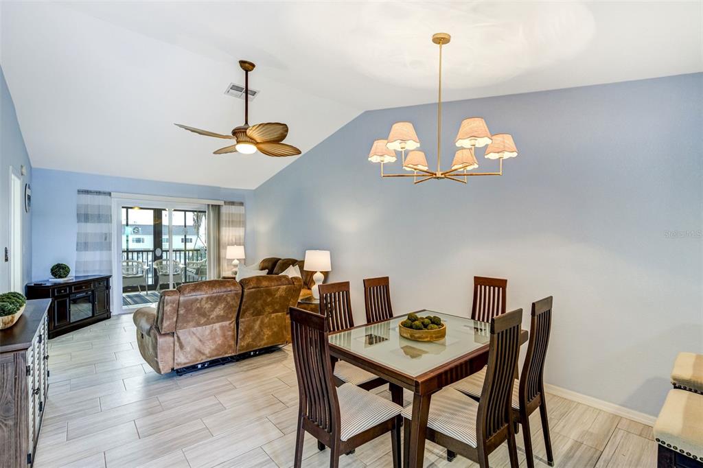 A dining area with a glass-topped table and chairs sits adjacent to a living room — 460 S PAULA DRIVE UNIT 108, DUNEDIN, FL