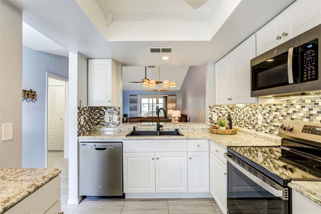 A kitchen features white cabinets, granite countertops, a mosaic tile backsplash, and stainless steel appliances — 460 S PAULA DRIVE UNIT 108, DUNEDIN, FL