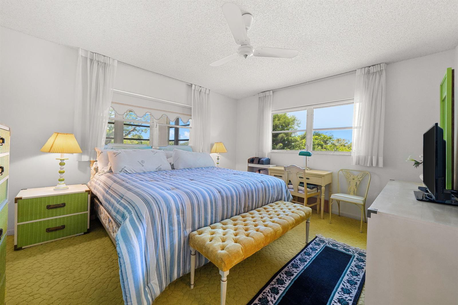 A bedroom features a bed with blue striped bedding, a yellow bench, and green nightstands — 2271 NW 48th Terrace # 207, Lauderhill FL 33313, LAUDERHILL, FL