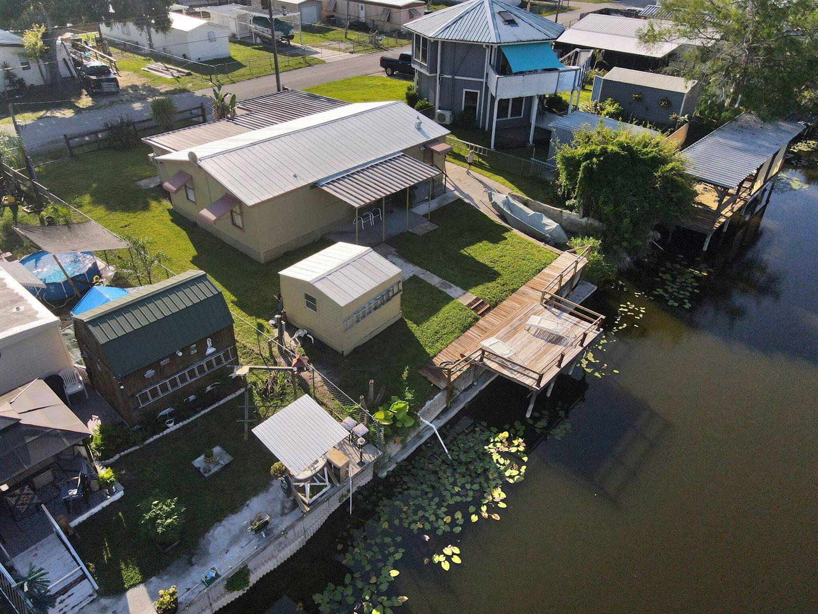 An aerial view shows a waterfront house with a wooden dock, sheds, and a pool — 1038 8th Street, Okeechobee FL 34974, OKEECHOBEE, FL