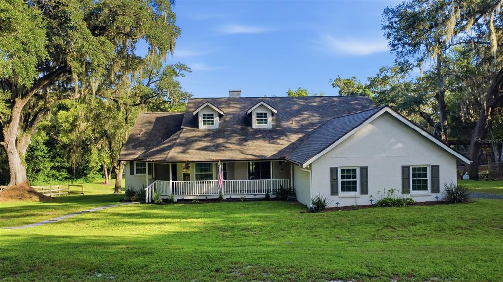 A two-story white house with a front porch and dormer windows sits on a lawn — 19832 W ELDORADO DRIVE, EUSTIS, FL