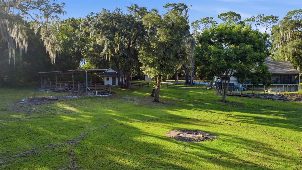 A grassy backyard features a covered outdoor structure, mature trees, and a residential house — 19832 W ELDORADO DRIVE, EUSTIS, FL