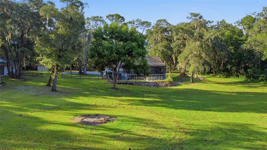 A large grassy backyard with a fire pit, mature trees, and a two-story house — 19832 W ELDORADO DRIVE, EUSTIS, FL