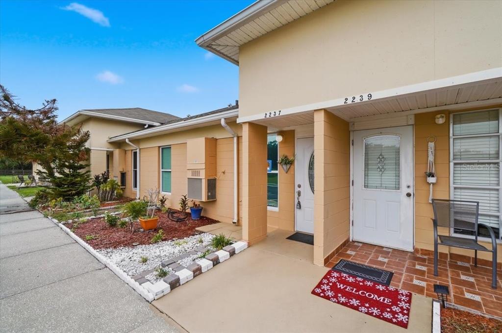 The exterior of a duplex features tan walls, two white front doors, and a landscaped yard — 2237 CLUB CIRCLE, LAKE WALES, FL