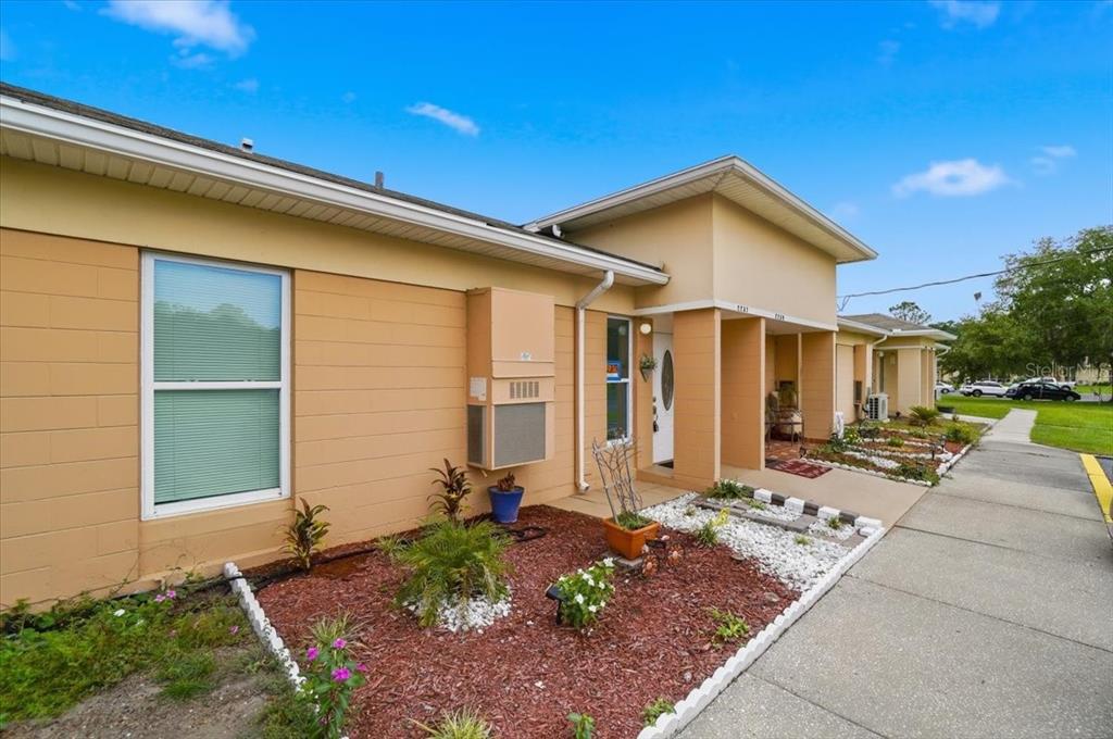 A single-story tan building with a white-trimmed window, a covered entrance, and landscaped garden beds — 2237 CLUB CIRCLE, LAKE WALES, FL