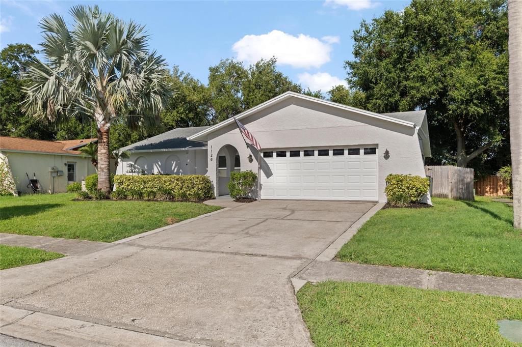 A single-story house with a white garage door, arched entryway, and a palm tree — 1128 FORBES TRACE, TARPON SPRINGS, FL