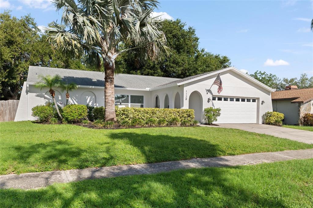 A single-story house with a white stucco exterior, a two-car garage, and a palm tree — 1128 FORBES TRACE, TARPON SPRINGS, FL