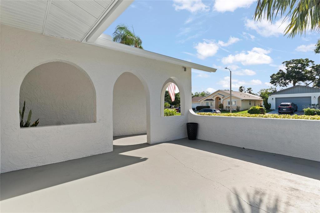 A covered patio features arched openings, a concrete floor, and a white stucco exterior wall — 1128 FORBES TRACE, TARPON SPRINGS, FL