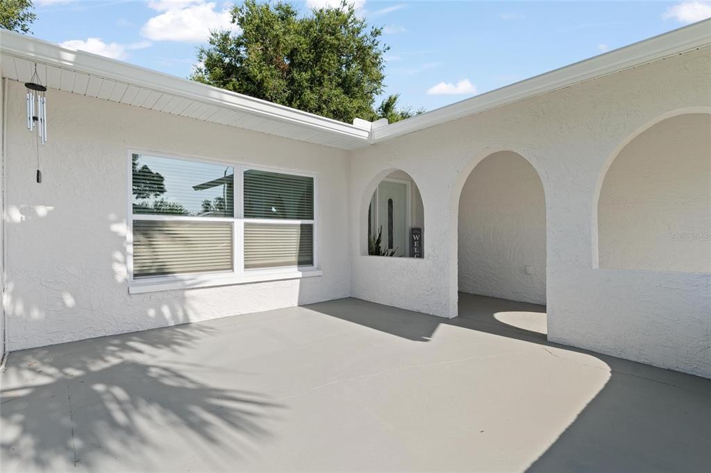 A covered patio area features white stucco walls, arched entryways, and a grey concrete floor — 1128 FORBES TRACE, TARPON SPRINGS, FL