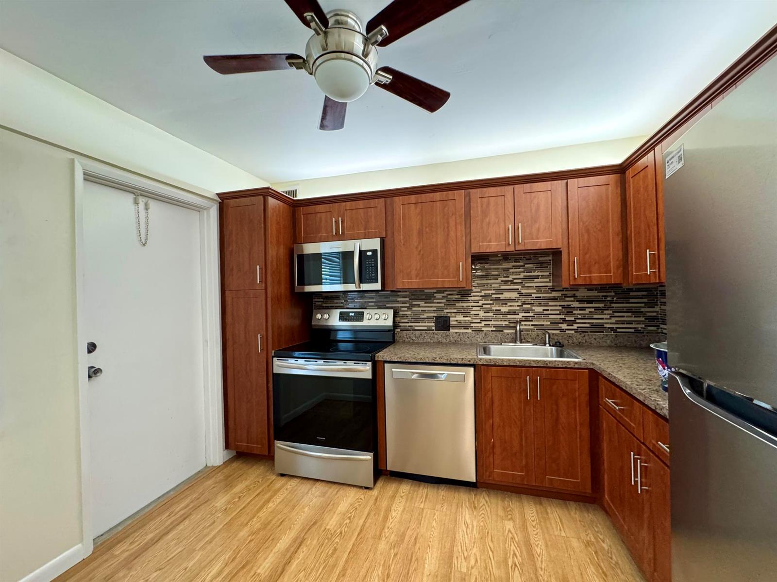 A kitchen features wood cabinets, stainless steel appliances, a tiled backsplash, and light wood flooring — 2650 S Course Drive # 407, Pompano Beach FL 33069, POMPANO BEACH, FL