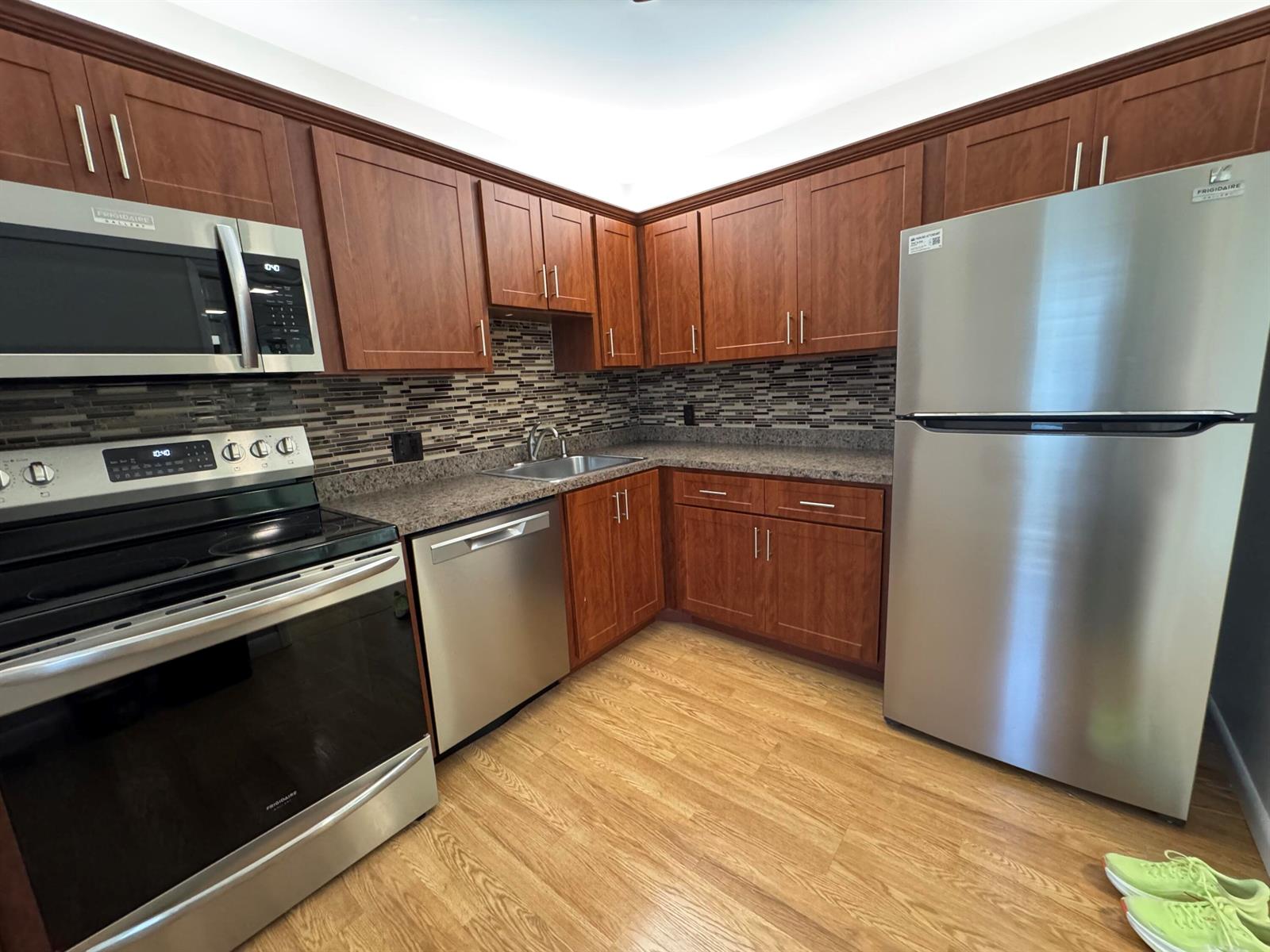 A kitchen features wood cabinets, stainless steel appliances, a mosaic backsplash, and light wood flooring — 2650 S Course Drive # 407, Pompano Beach FL 33069, POMPANO BEACH, FL