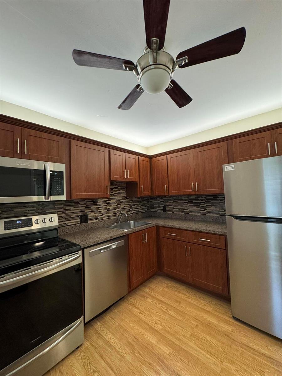 A kitchen features wood cabinets, stainless steel appliances, granite countertops, and a ceiling fan — 2650 S Course Drive # 407, Pompano Beach FL 33069, POMPANO BEACH, FL