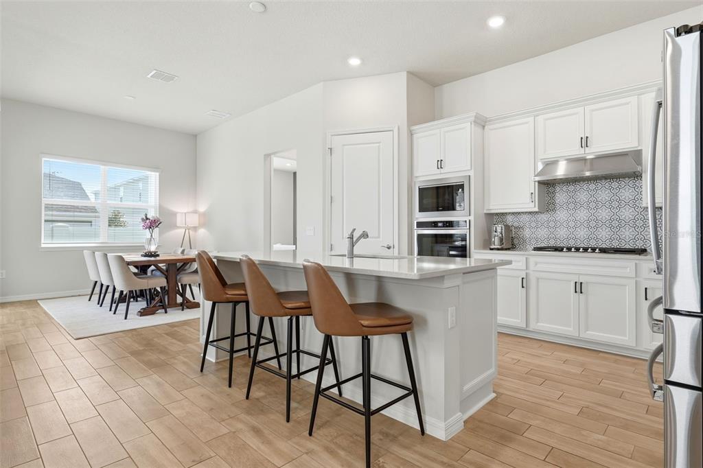 A kitchen with white cabinets, a quartz island, and bar stools next to a dining area — 10325 PARKVIEW RESERVE LANE, ORLANDO, FL