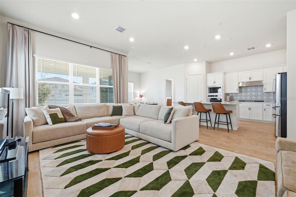 An open-concept living room features a large sectional sofa, patterned rug, and adjacent kitchen — 10325 PARKVIEW RESERVE LANE, ORLANDO, FL