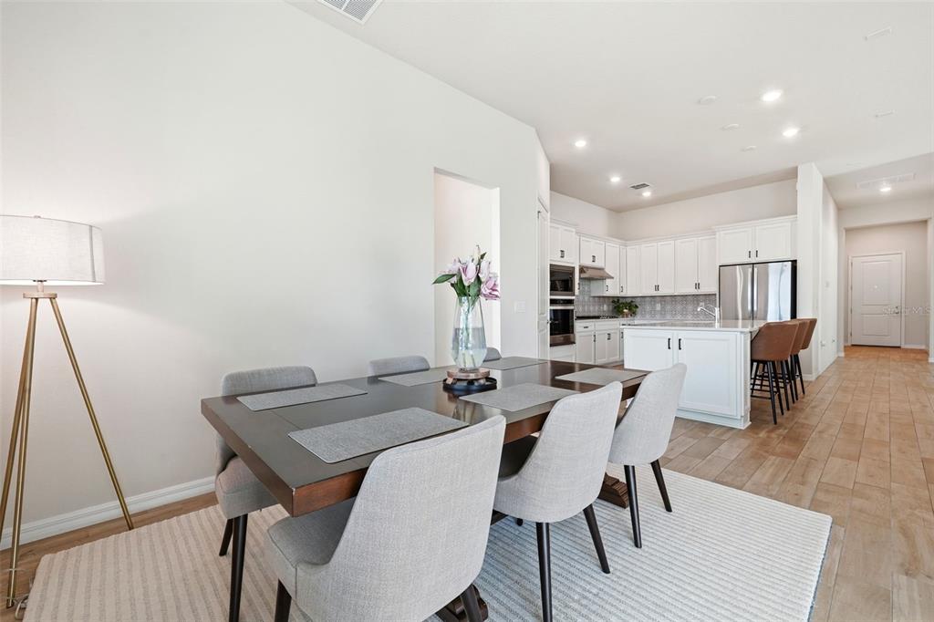 A dining area with a dark wood table and gray chairs sits before an open kitchen — 10325 PARKVIEW RESERVE LANE, ORLANDO, FL