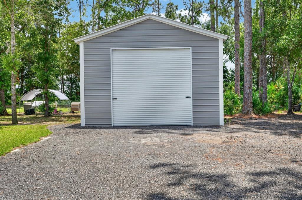 A gray metal storage shed with a white roll-up garage door sits on a gravel lot — 4825 PECAN AVENUE, BUNNELL, FL