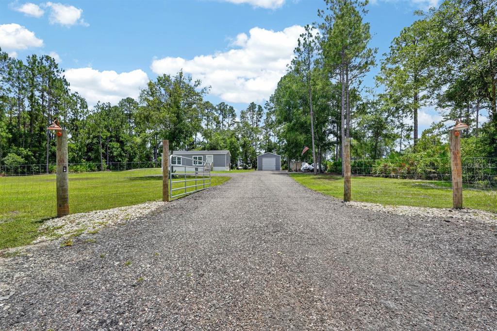 A gravel driveway leads through a gated entrance toward a house and detached garage — 4825 PECAN AVENUE, BUNNELL, FL