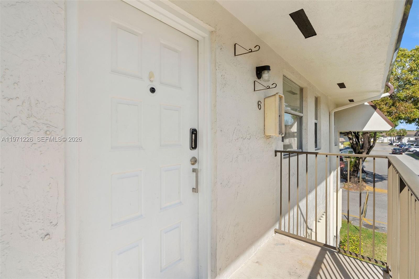 A white front door with a digital lock is located on an outdoor balcony — 7111 SW 129th Ave # 6, Miami FL 33183, MIAMI, FL