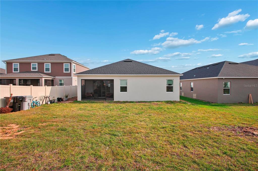 The rear exterior of a single-story house features a screened-in patio and a grassy yard — 900 POINTE EMERSON BOULEVARD, APOPKA, FL