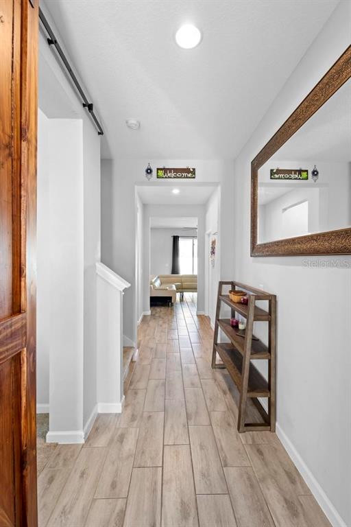 A hallway with wood-look tile flooring leads toward a living area with a wooden shelf — 3565 FERNANDA DRIVE, DELTONA, FL