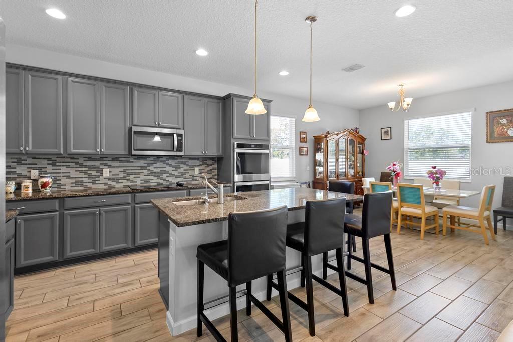 A kitchen features gray cabinets, granite countertops, a center island with bar stools, and tile flooring — 3565 FERNANDA DRIVE, DELTONA, FL