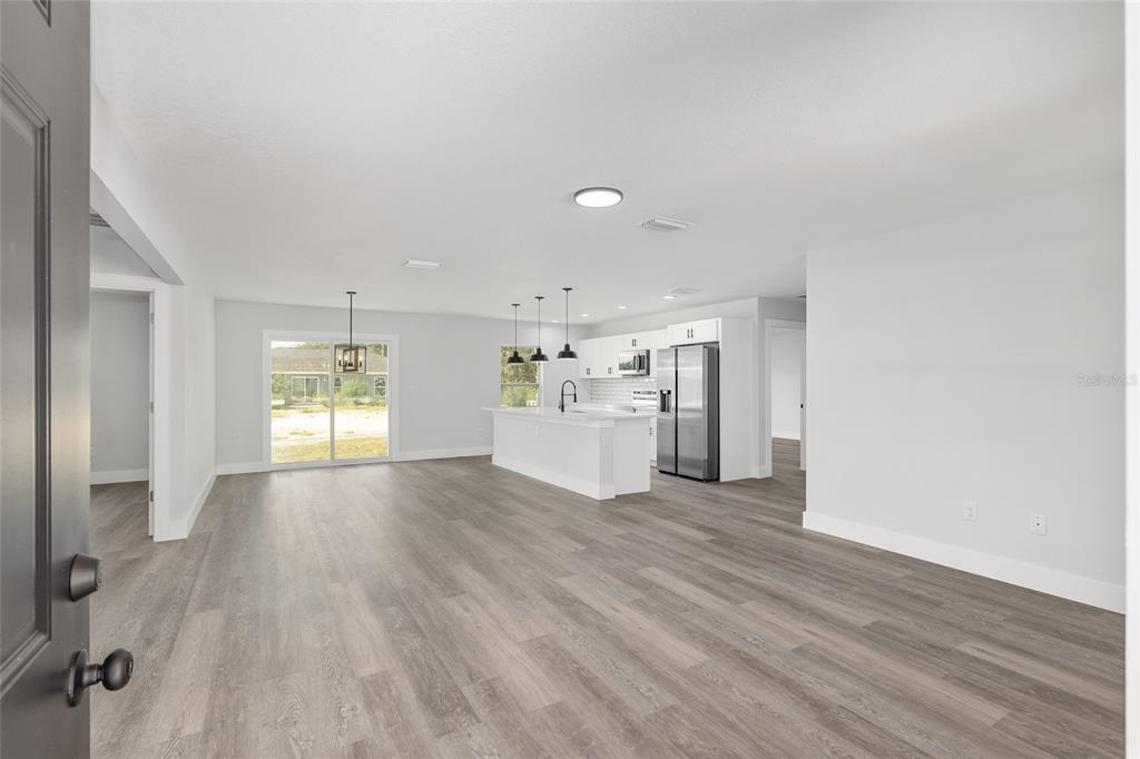 A living room features gray wood-look flooring, a gray sofa, and a wall-mounted television — 2495 SW 141ST COURT, OCALA, FL