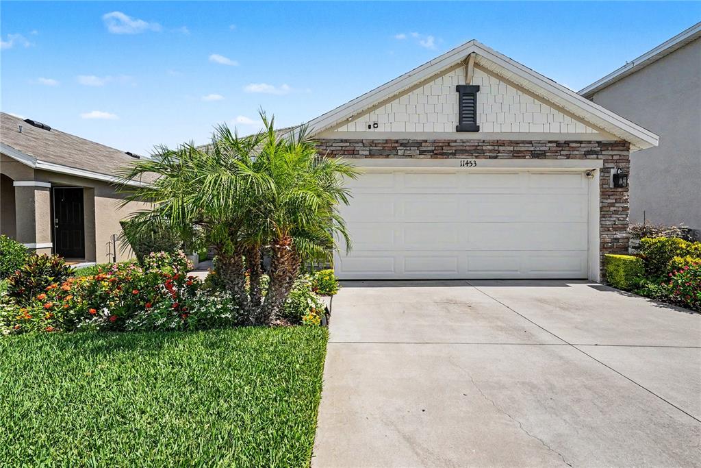 A single-story house exterior features a two-car garage, stone facade, and a palm tree — 11453 STONE PINE STREET, RIVERVIEW, FL