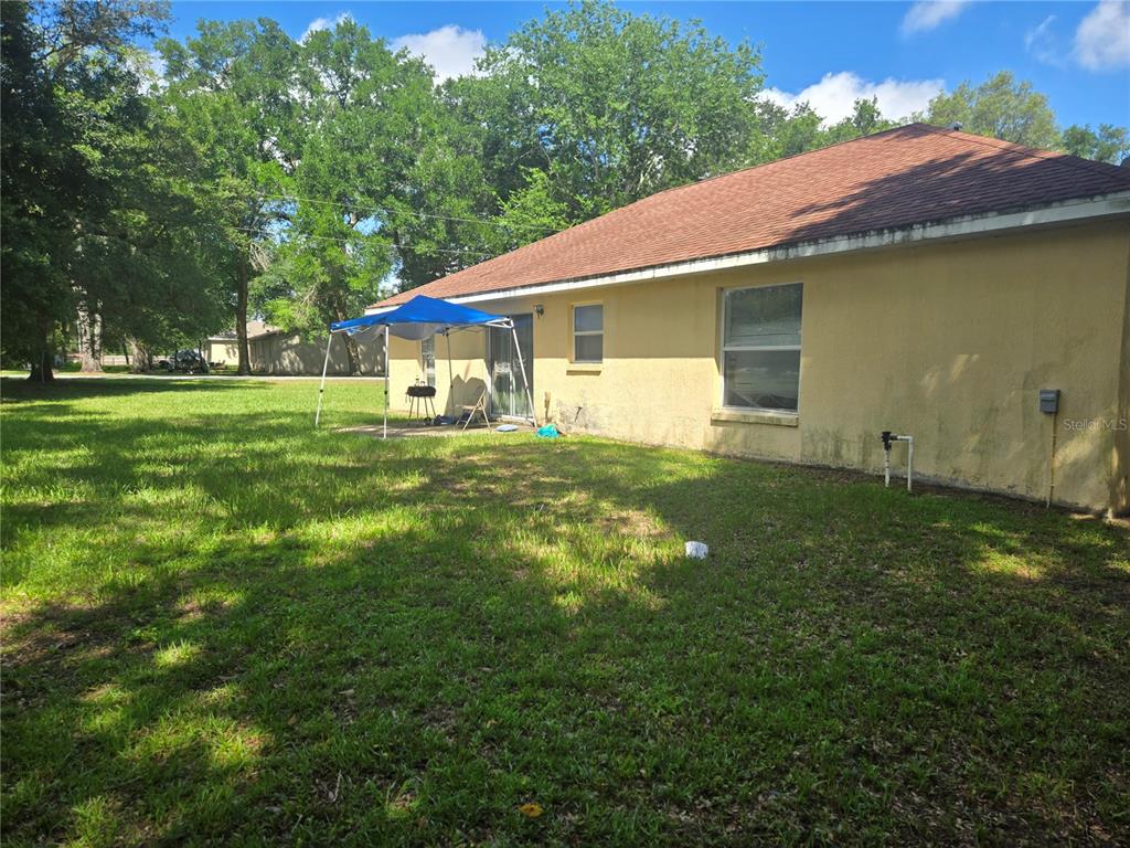 The exterior of a yellow stucco house features a blue canopy on the back lawn — 31 PINE CIRCLE, OCALA, FL