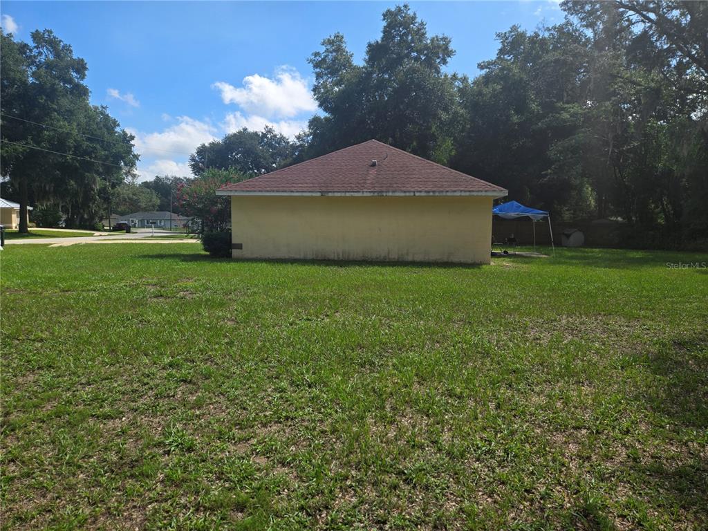 A view of a yellow house exterior with a hip roof and a large lawn — 31 PINE CIRCLE, OCALA, FL