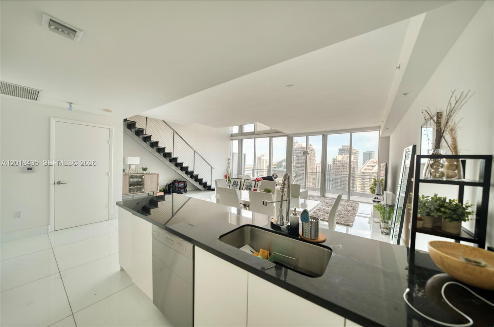 A modern kitchen with black countertops overlooks a bright living area with a staircase — 92 SW 3rd St # 5203, Miami FL 33130, MIAMI, FL