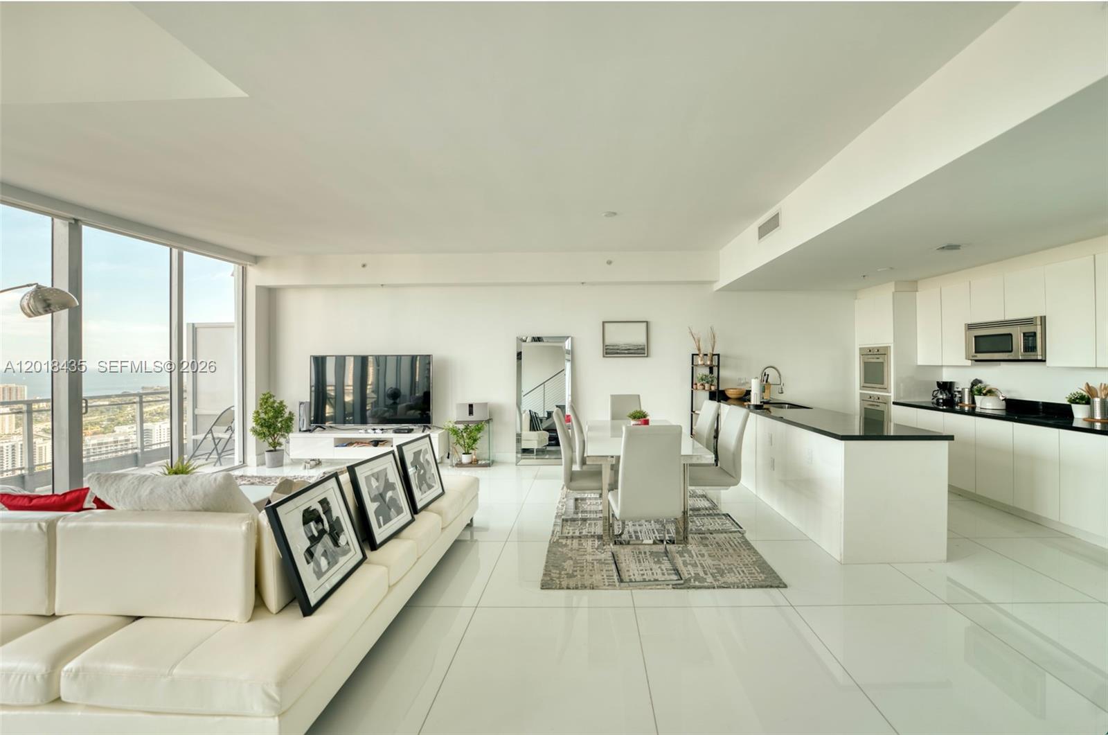 A modern open-concept living and dining area features white tile floors and a sleek kitchen — 92 SW 3rd St # 5203, Miami FL 33130, MIAMI, FL