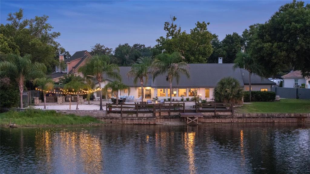 A waterfront house with a patio, string lights, palm trees, and a wooden dock — 2201 COVE COURT, LONGWOOD, FL