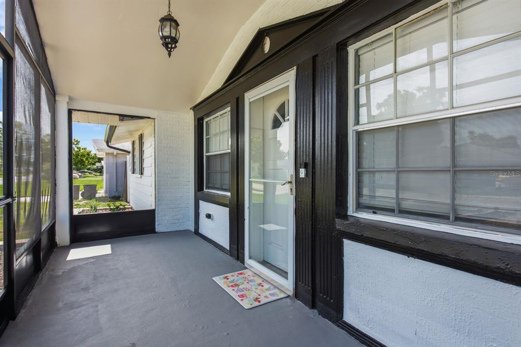 A covered porch features a gray floor, white brick walls, and a black-framed front door — 7631 HOLLYRIDGE DRIVE, NEW PORT RICHEY, FL