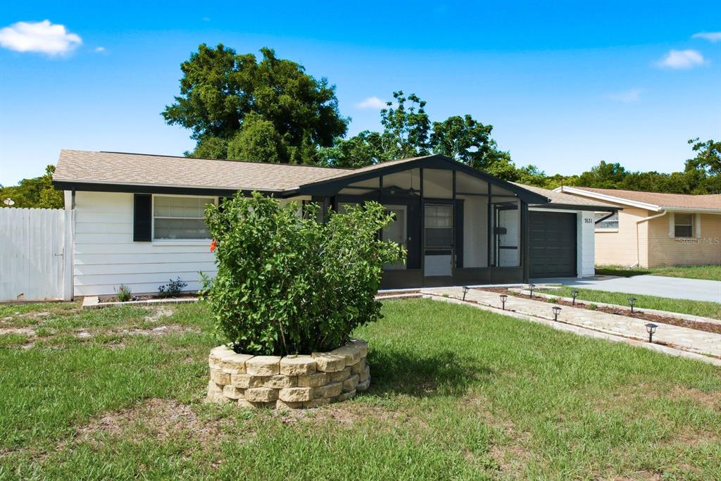 A single-story house with white siding, a screened front porch, and a stone-bordered bush — 7631 HOLLYRIDGE DRIVE, NEW PORT RICHEY, FL