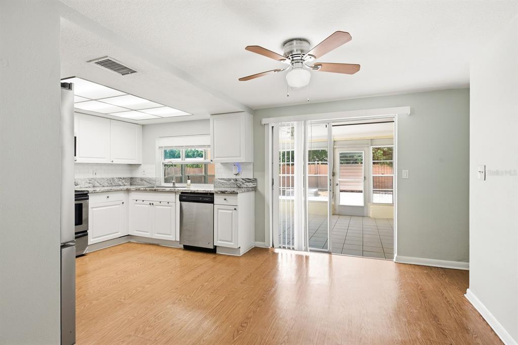 A kitchen with white cabinets and stainless steel appliances opens to a tiled sunroom — 7631 HOLLYRIDGE DRIVE, NEW PORT RICHEY, FL