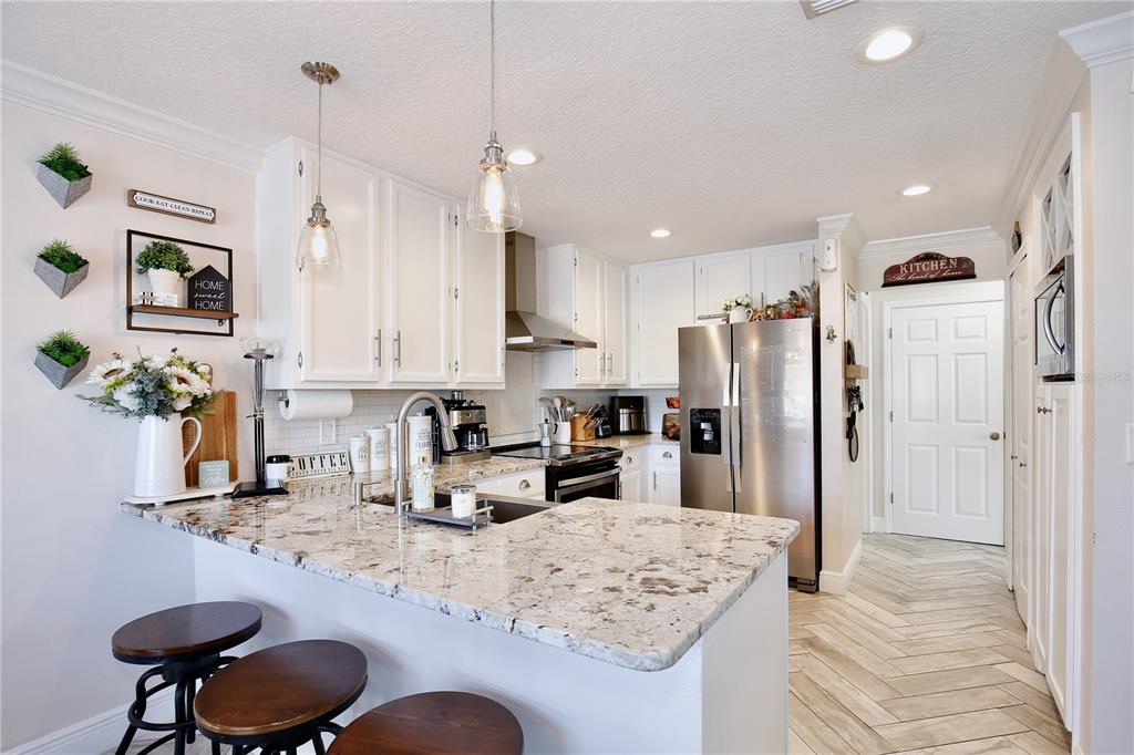 A kitchen with white cabinets, granite countertops, stainless steel appliances, and three bar stools — 2115 HEATHWOOD CIRCLE, ORLANDO, FL