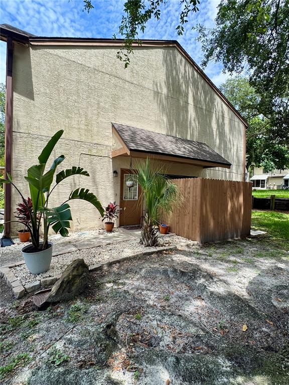A tan stucco building exterior features a brown wooden privacy fence and potted plants — 2504 BRIGADOON DRIVE, CLEARWATER, FL