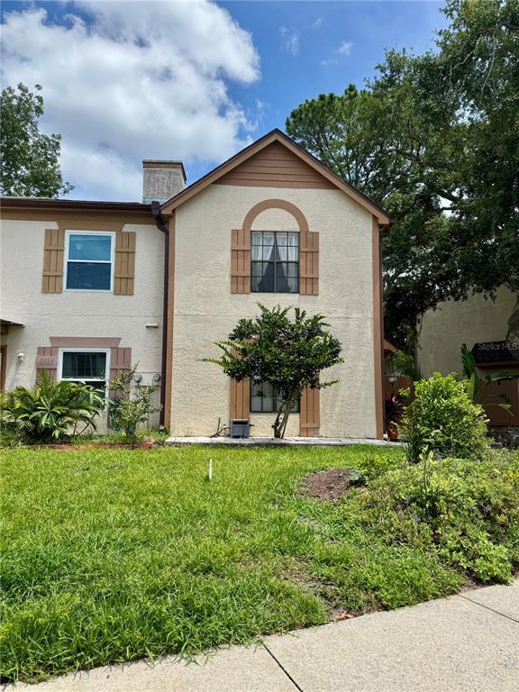 A two-story stucco townhouse features brown shutters, a small tree, and a grassy front yard — 2504 BRIGADOON DRIVE, CLEARWATER, FL