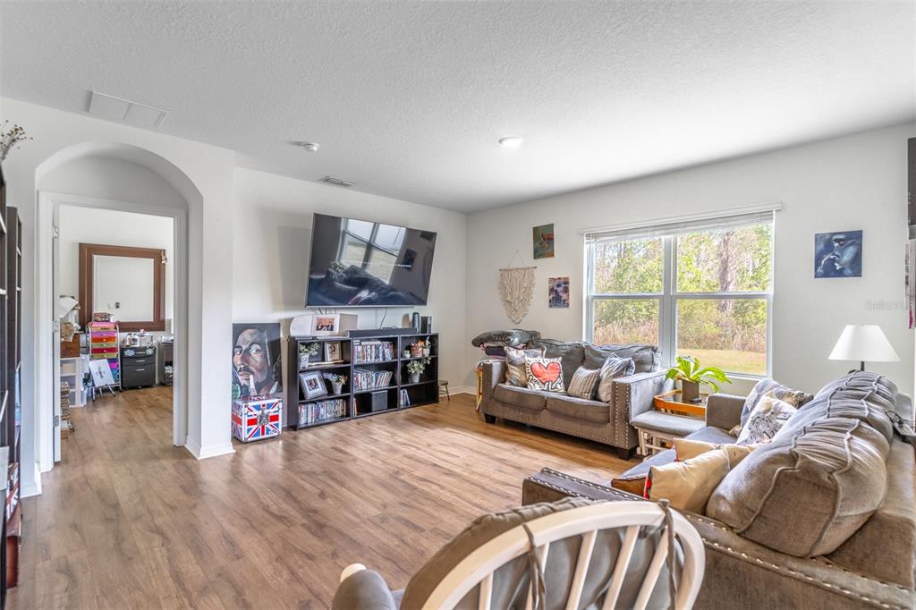 A living room features wood-look flooring, a wall-mounted television, a bookshelf, and two gray sofas — 1419 FOX SQUIRREL DRIVE, DAVENPORT, FL