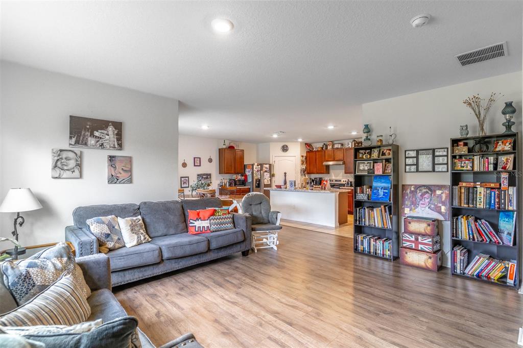A living room with wood-look flooring, a gray sofa, and an open kitchen in the background — 1419 FOX SQUIRREL DRIVE, DAVENPORT, FL