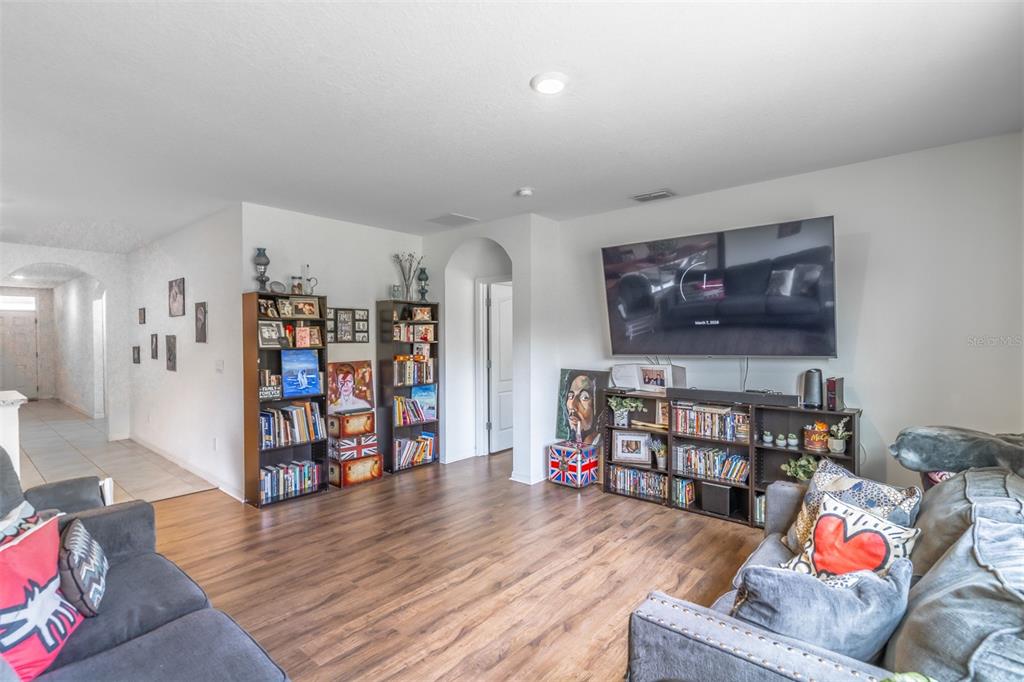 A living room with wood-look flooring, two bookshelves, and a wall-mounted television — 1419 FOX SQUIRREL DRIVE, DAVENPORT, FL