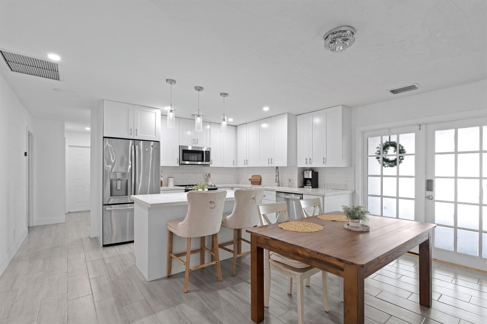 A modern kitchen features white cabinetry, stainless steel appliances, a center island, and a dining table — 5285 Sunrise Boulevard, Delray Beach FL 33484, DELRAY BEACH, FL