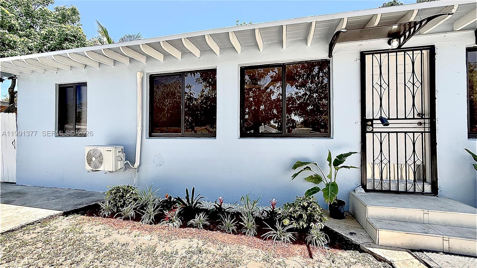 The exterior of a light blue house features a metal security door and small windows — 1352 NW 112th Ter, Miami FL 33167, MIAMI, FL