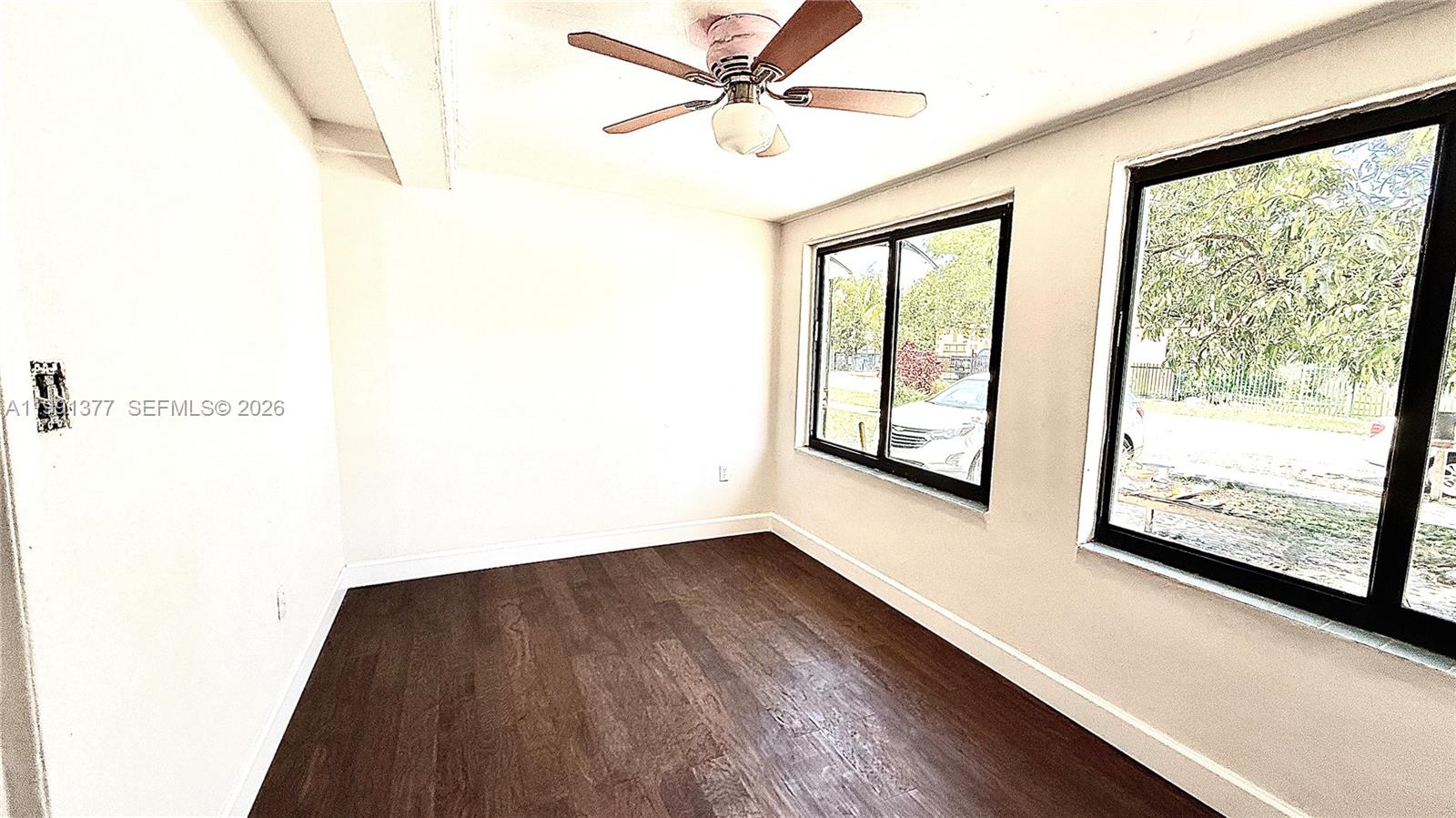 An empty room features dark wood flooring, white walls, two windows, and a ceiling fan — 1352 NW 112th Ter, Miami FL 33167, MIAMI, FL