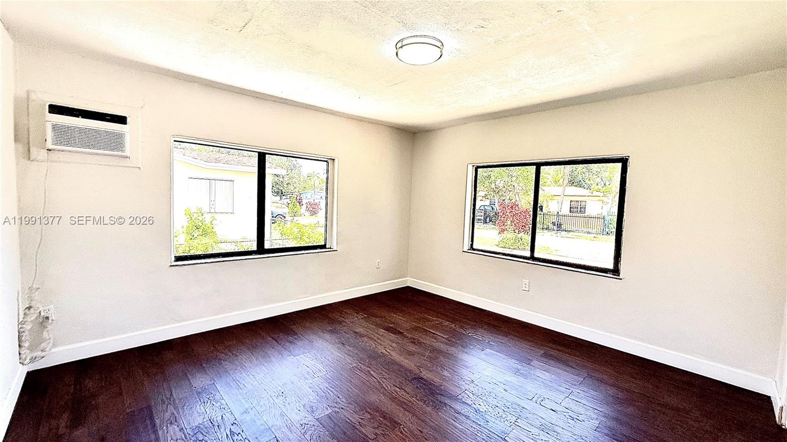 An empty room features dark wood flooring, white walls, two windows, and a wall-mounted air conditioner — 1352 NW 112th Ter, Miami FL 33167, MIAMI, FL