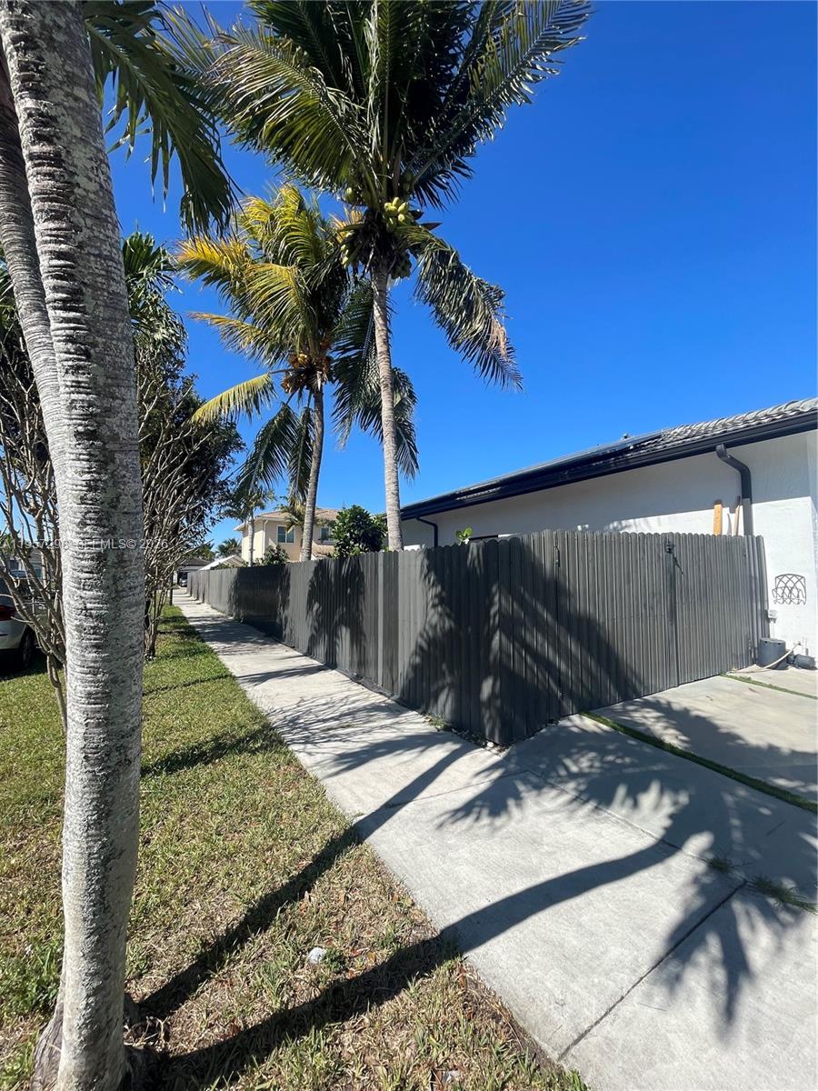 A gray wooden fence runs along a concrete sidewalk next to a palm tree — 14200 SW 160th Ct, Miami FL 33196, MIAMI, FL