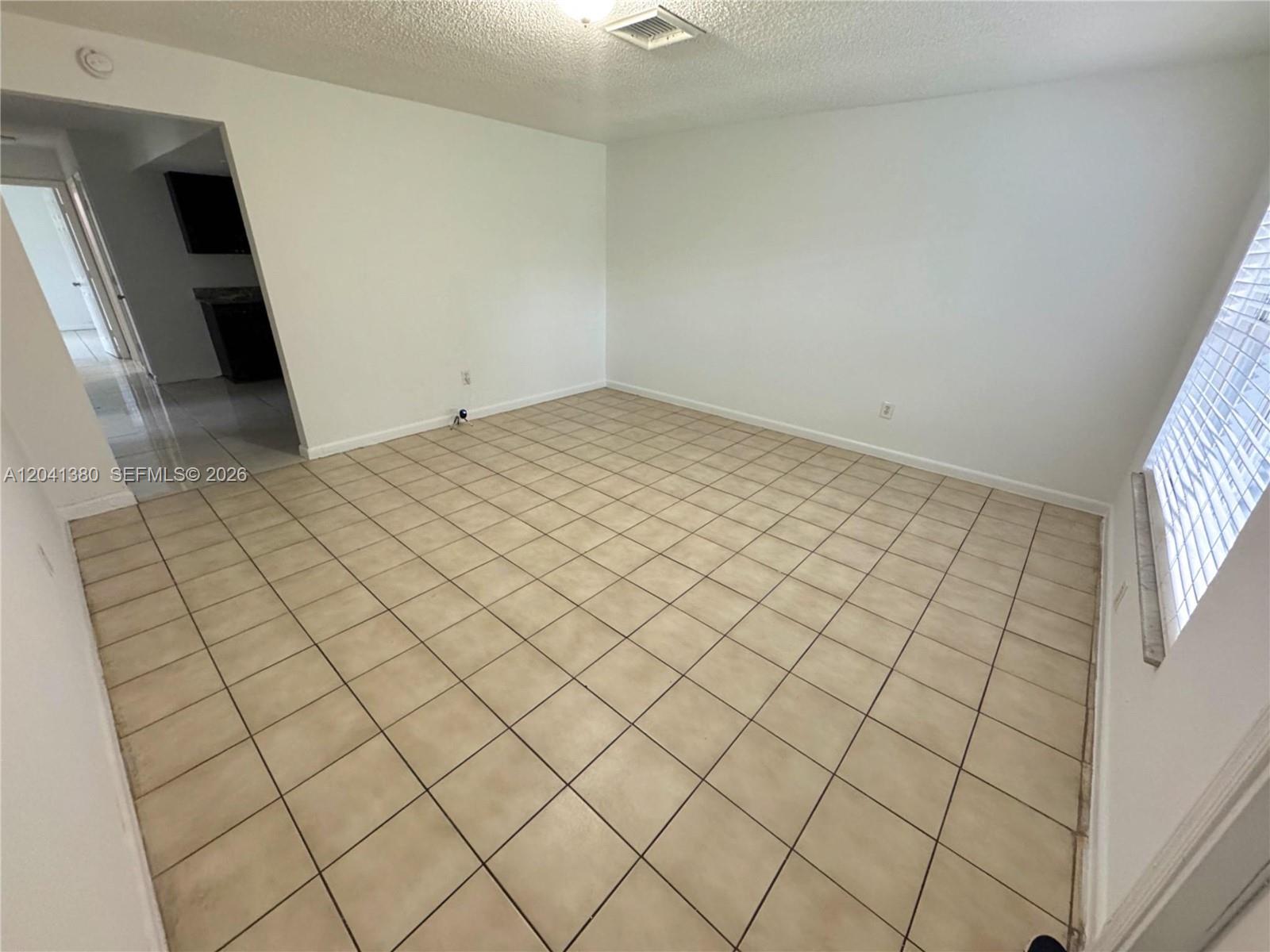 An empty room features beige square floor tiles, white walls, and a window with blinds — NORTH LAUDERDALE, FL