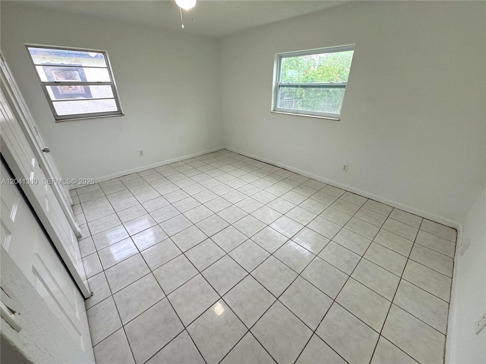 An empty bedroom features white walls, tile flooring, and two windows — NORTH LAUDERDALE, FL