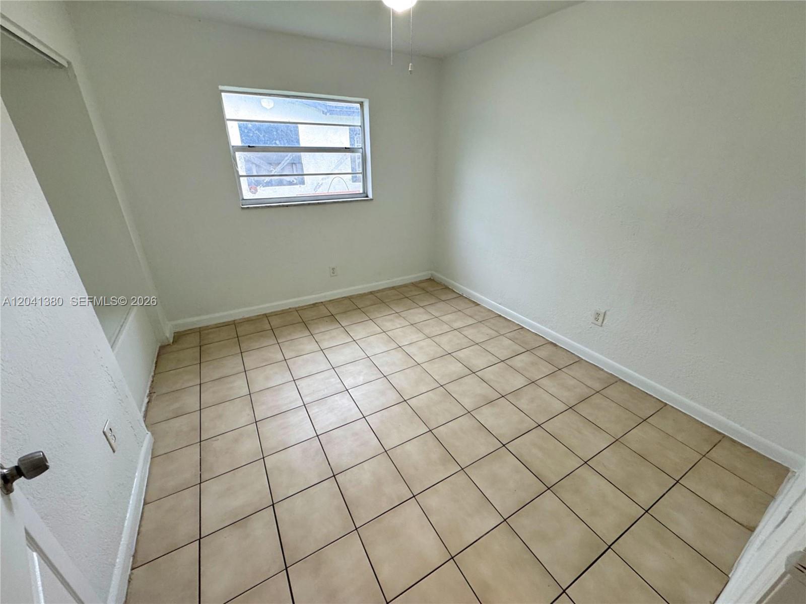 An empty room features white walls, a single window, and beige square floor tiles — NORTH LAUDERDALE, FL