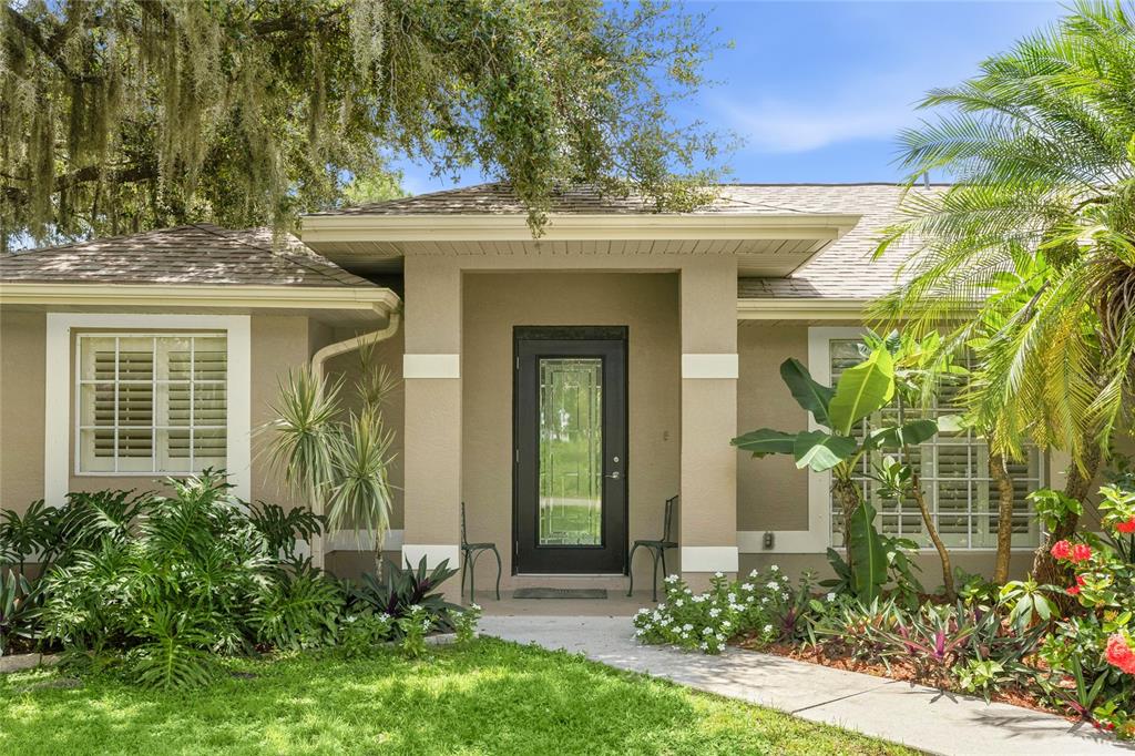 The front exterior of a tan house features a dark glass door and lush landscaping — 2451 ALTOONA AVENUE, NORTH PORT, FL